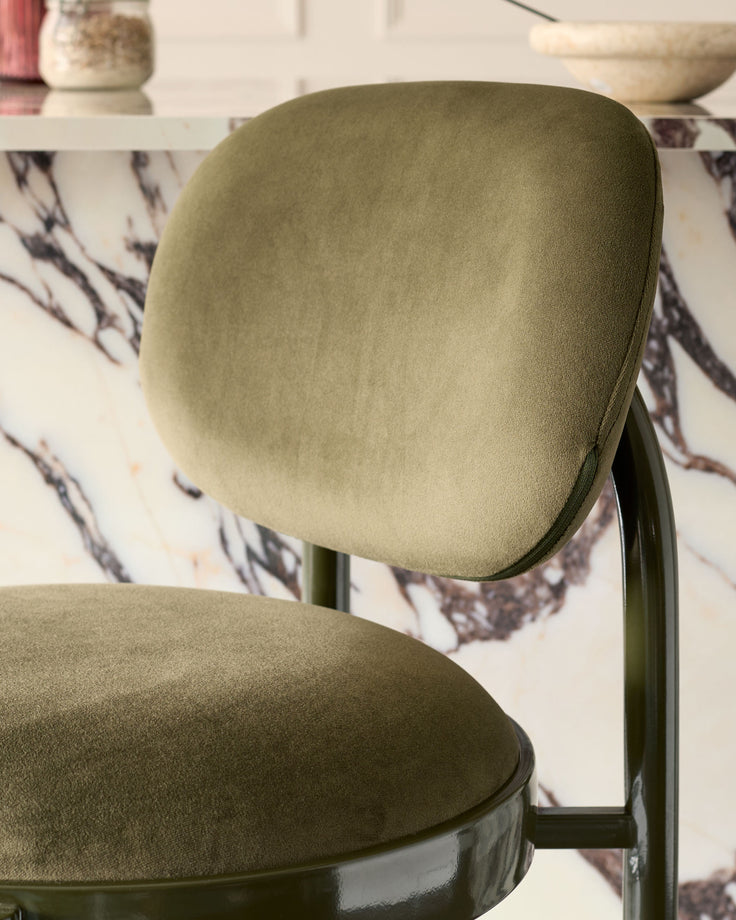 Blake bar stool in olive green velvet with curved backrest and metal frame, shown from side angle.
