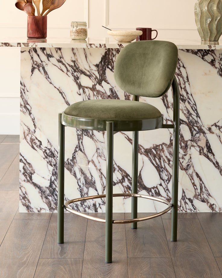 Blake bar stool in olive green velvet with metal frame and footrest, positioned at marble counter.