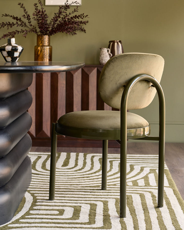 Blake dining chair in olive green velvet with curved backrest and metal frame, shown in room setting.