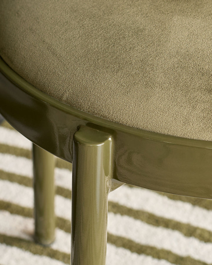Close-up of Blake dining chair's olive green velvet seat and metal leg detail on striped rug.