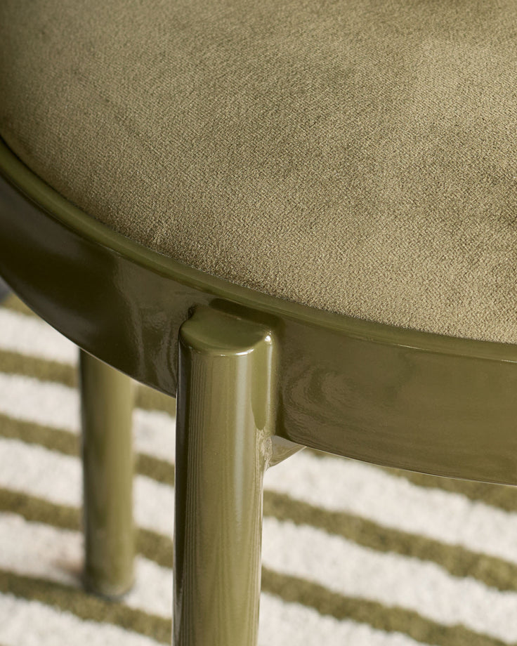 Close-up of Blake dining chair's olive green velvet seat and metal leg detail on striped rug.