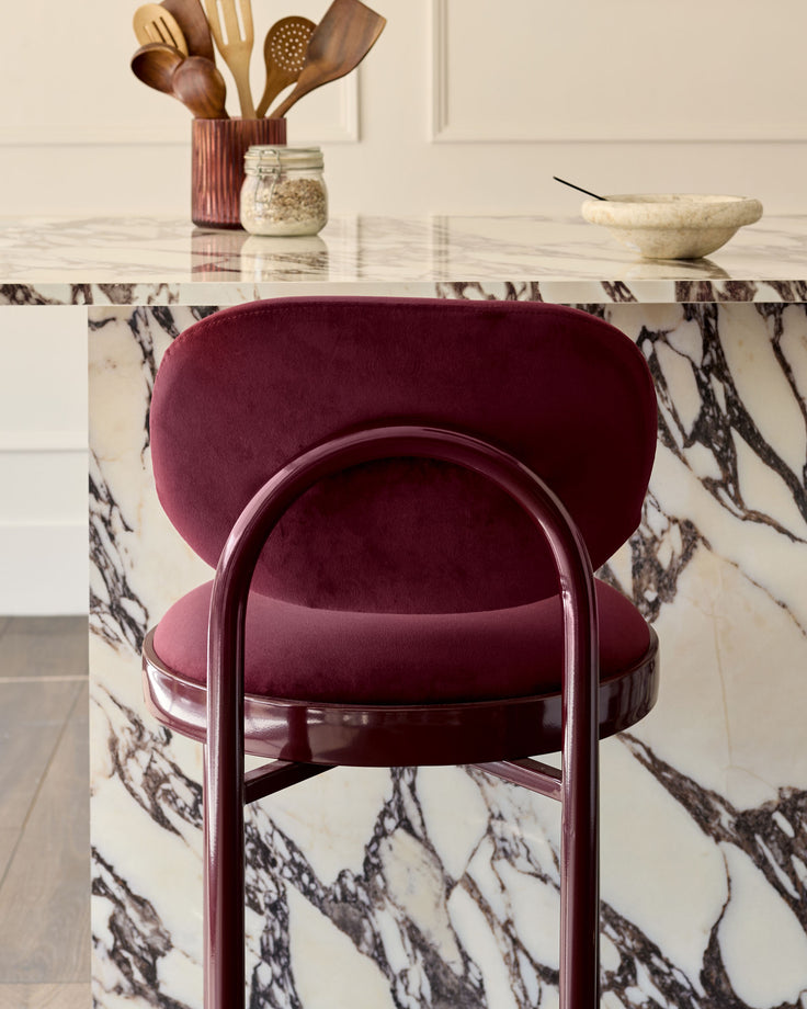 Blake bar stool in plum velvet with curved backrest and metal frame, shown at marble-patterned counter.