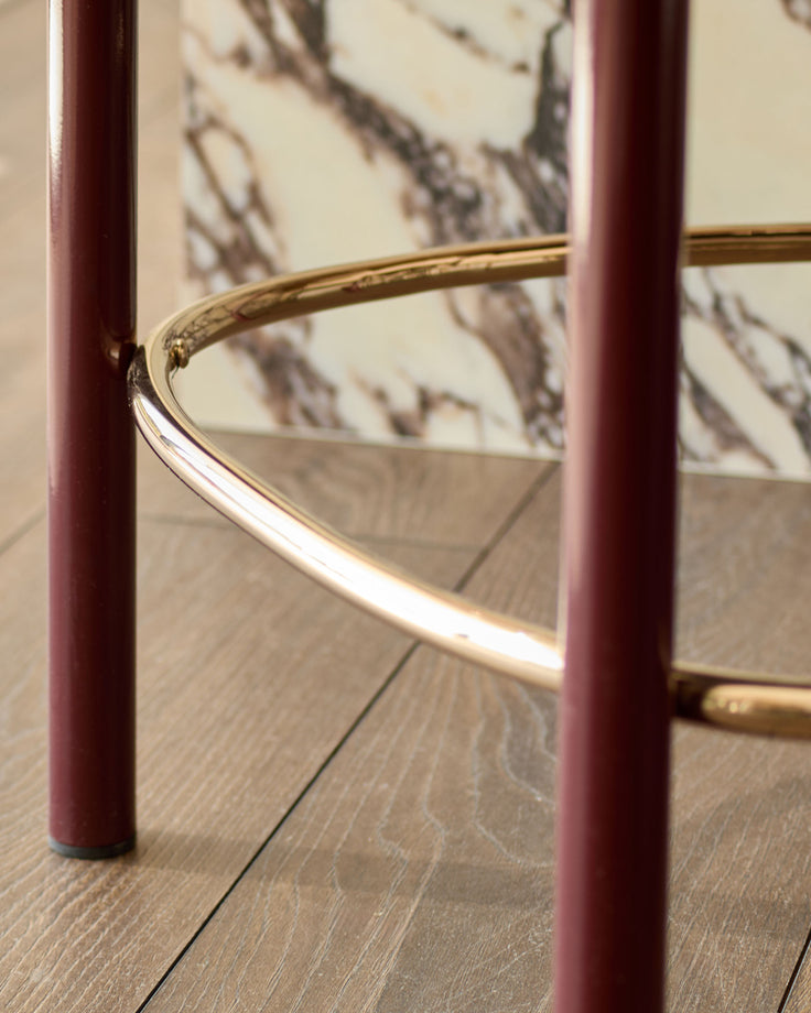 Blake bar stool in plum velvet with brass footrest detail, shown on wood flooring from a side angle.