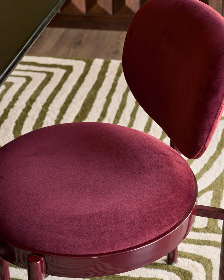 Blake dining chair in plum velvet with rounded seat and backrest, shown on striped area rug.