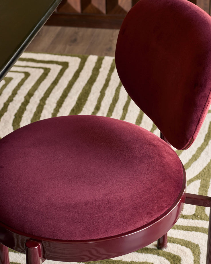 Blake dining chair in plum velvet with rounded seat and backrest, shown on striped area rug.