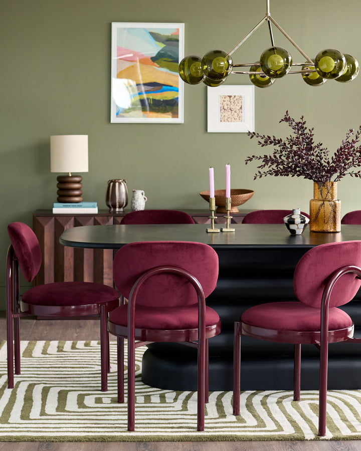 Blake dining chair in plum velvet with curved backrest and metal frame, shown in sage green dining room setting.