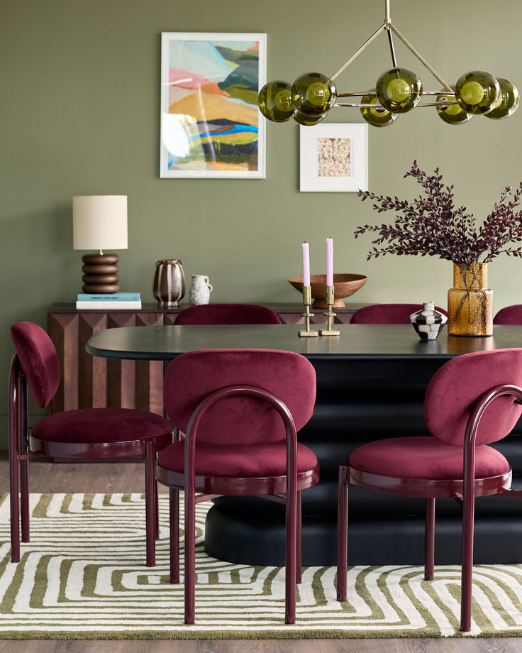 Blake dining chair in plum velvet with curved backrest and metal frame, shown in sage green dining room setting.
