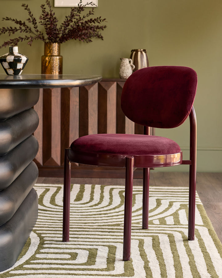Blake dining chair in plum velvet with wooden legs, shown in styled room setting beside round table.