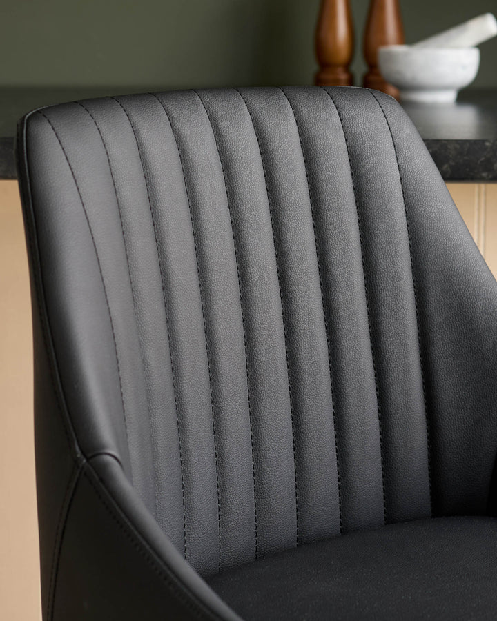 Black faux leather bar stool with vertical channel stitching detail on backrest, shown at angle.