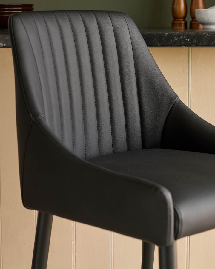 Black faux leather bar stool with vertical stitched backrest detail, shown from side angle at counter.