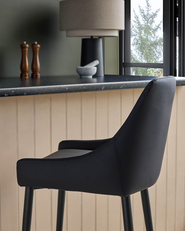 Blakely bar stool in black faux leather, shown from side angle at a kitchen counter with dark marble top.