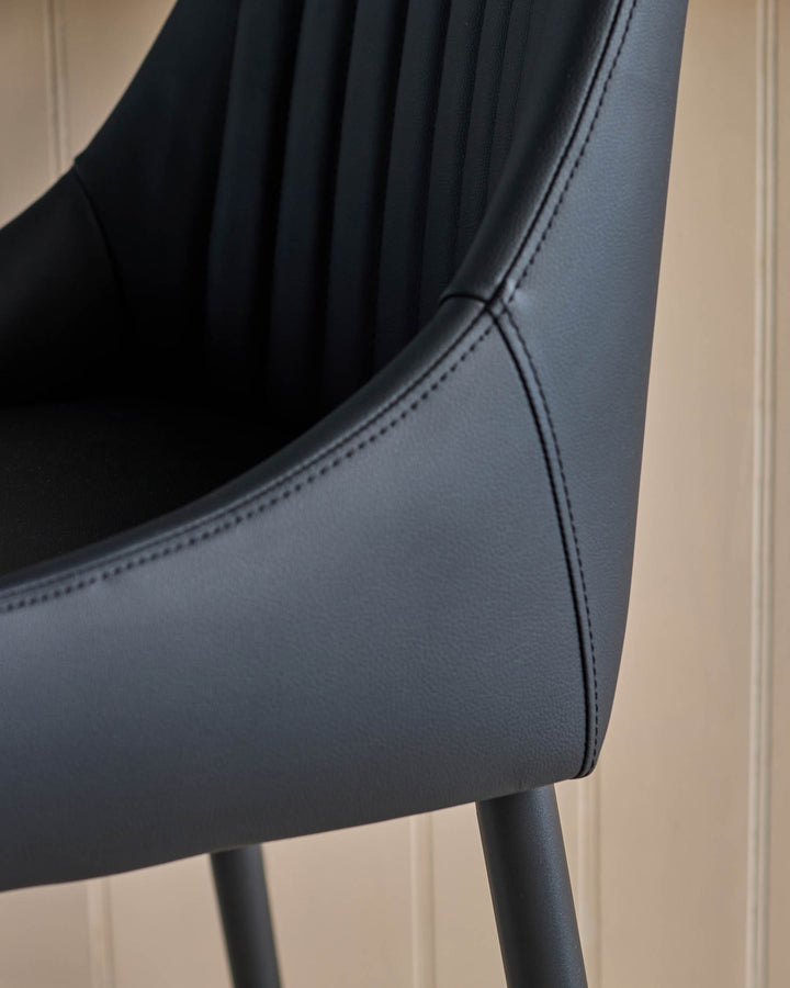 Black faux leather bar stool featuring vertical stitching detail, curved backrest, and metal legs, angled side view.