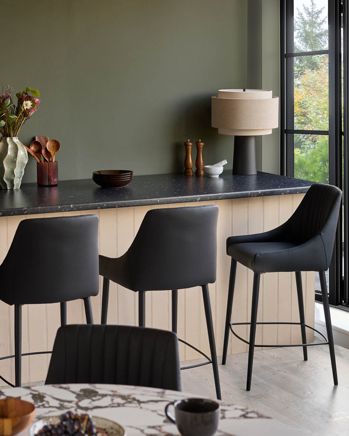 Blakely black faux leather bar stools with curved backs and metal footrests, shown at a kitchen island counter.