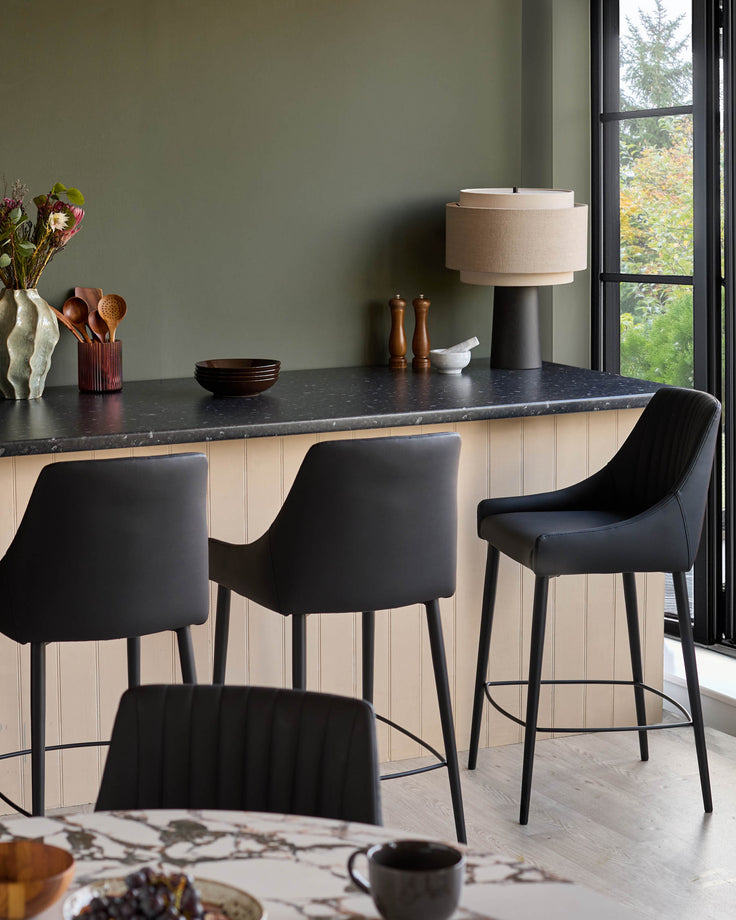 Blakely black faux leather bar stools with curved backs and metal footrests, shown at a kitchen island counter.