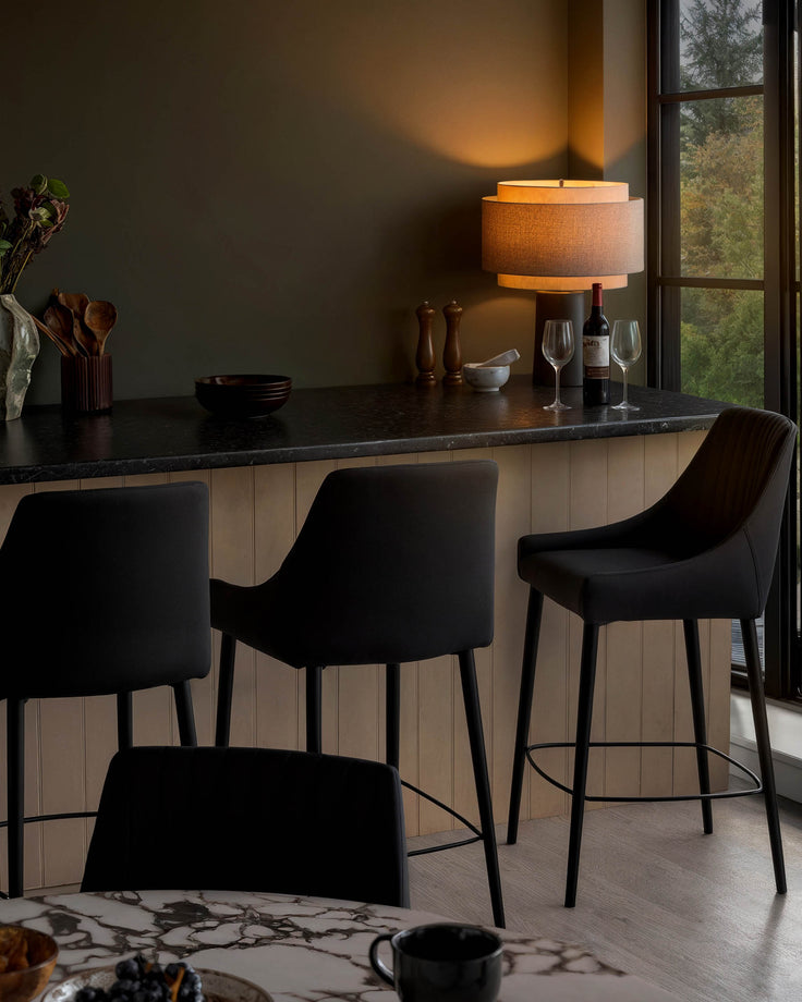 Blakely black faux leather bar stools with curved backs and metal footrests, shown at a kitchen counter.