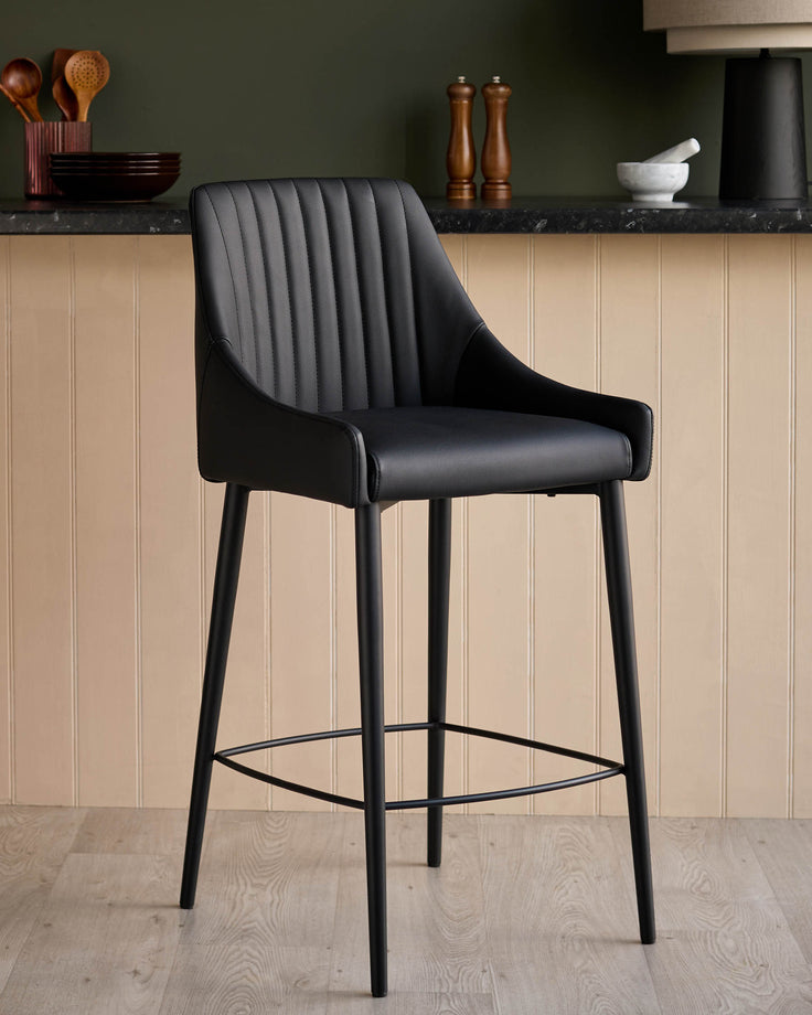 Black faux leather bar stool with vertical stitched backrest, black metal legs, and footrest in modern kitchen setting.