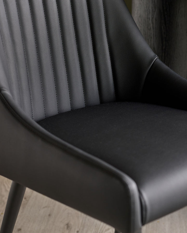 Black faux leather dining chair with vertical pleated backrest detail and curved seat, angled view.