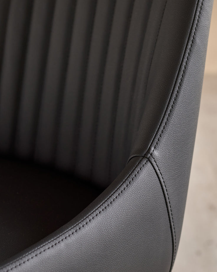 Close-up of black faux leather dining chair showing vertical quilted stitching and curved seam detail.