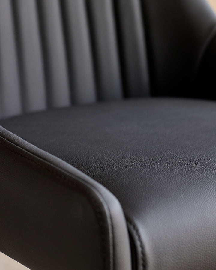 Blakely faux-leather dining chair in black, close-up showing textured seat surface and curved armrest detail.