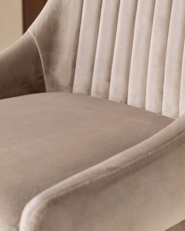 Close-up of a light beige velvet chair with armrests and a vertically channelled backrest.