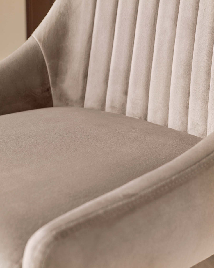 Close-up of a light beige velvet chair with armrests and a vertically channelled backrest.