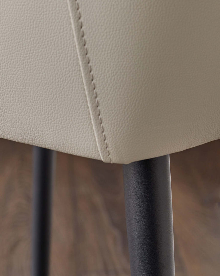 Close-up of a chair with light grey leather upholstery and black metal legs, showcasing texture and design details.