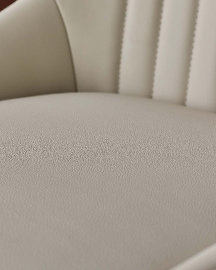 Close-up of a cream upholstered chair seat with a textured leather look and fluted back, ideal for a modern home.