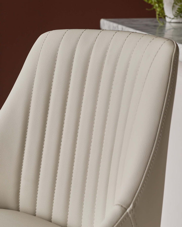 Close-up of a cream leather chair with vertical stitching, exuding comfort and style.