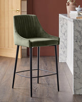 Blakely bar stool in olive green velvet with vertical stitching, black metal legs and footrest.
