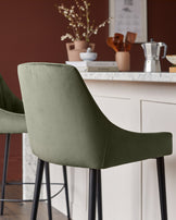 Blakely bar stool in olive green velvet with black legs, shown from behind at a kitchen counter.