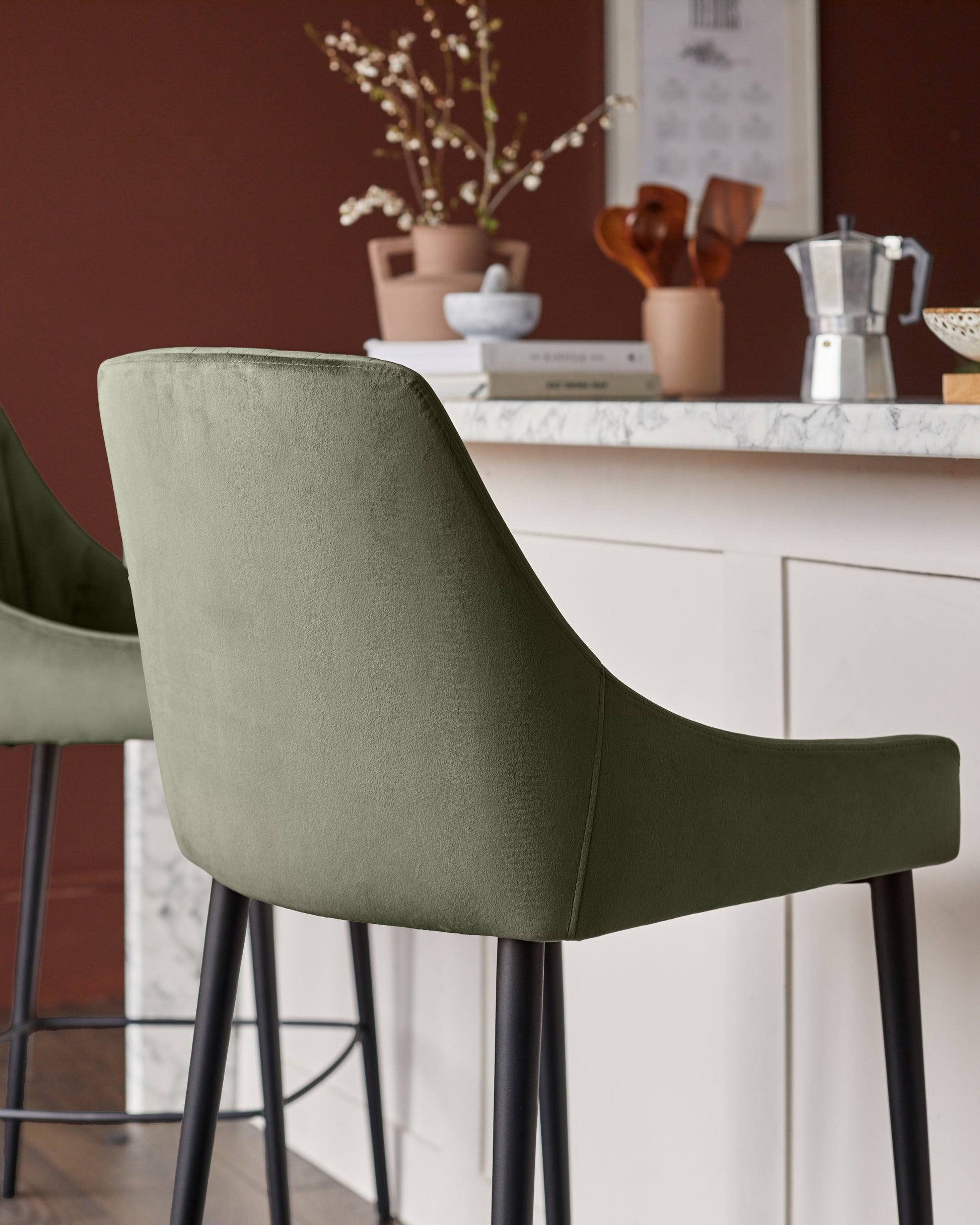 Blakely bar stool in olive green velvet with black legs, shown from behind at a kitchen counter.