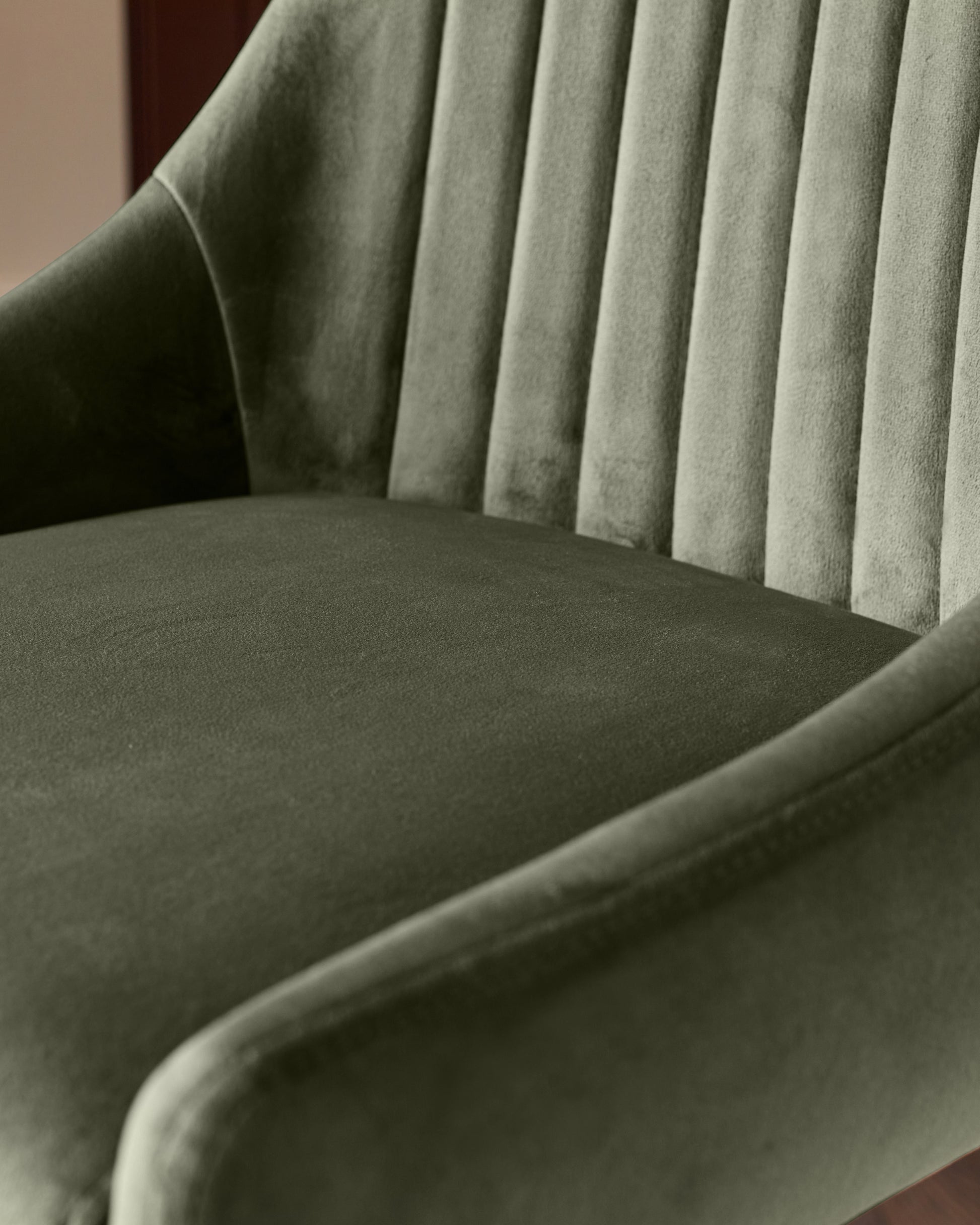 Blakely bar stool in olive green velvet, showing pleated backrest and curved seat from side angle.