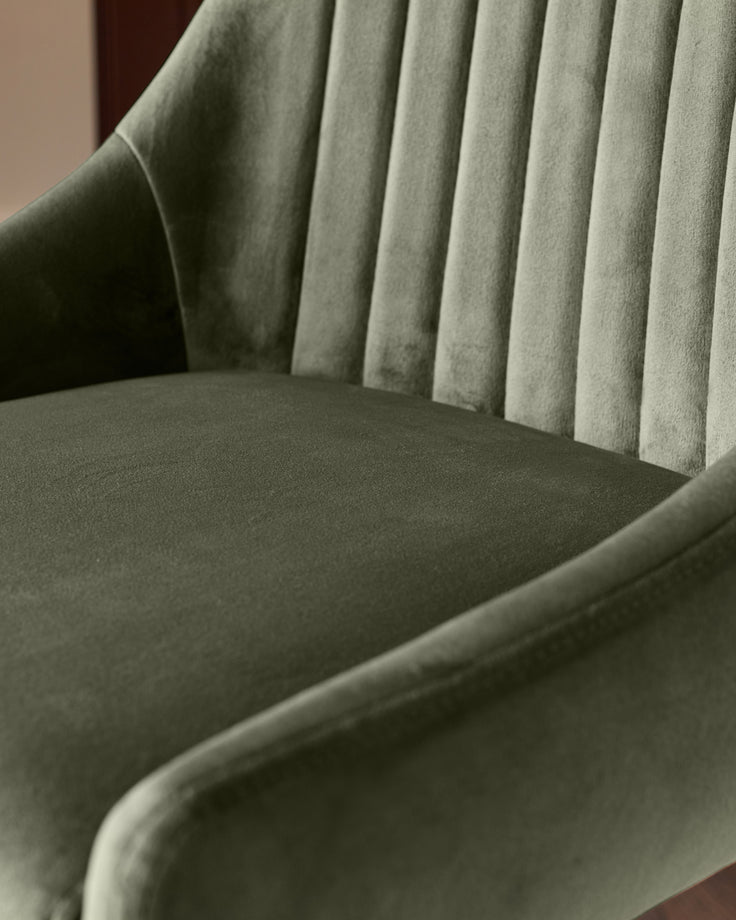 Blakely bar stool in olive green velvet, showing pleated backrest and curved seat from side angle.