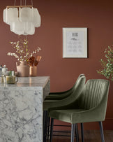 Blakely bar stool in olive green velvet with vertical channel stitching and dark wood legs, shown at marble counter.