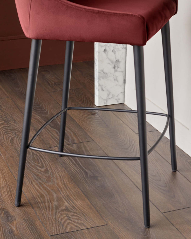 Close-up of a stool with a burgundy seat and black metal legs, showcasing its design and materials.