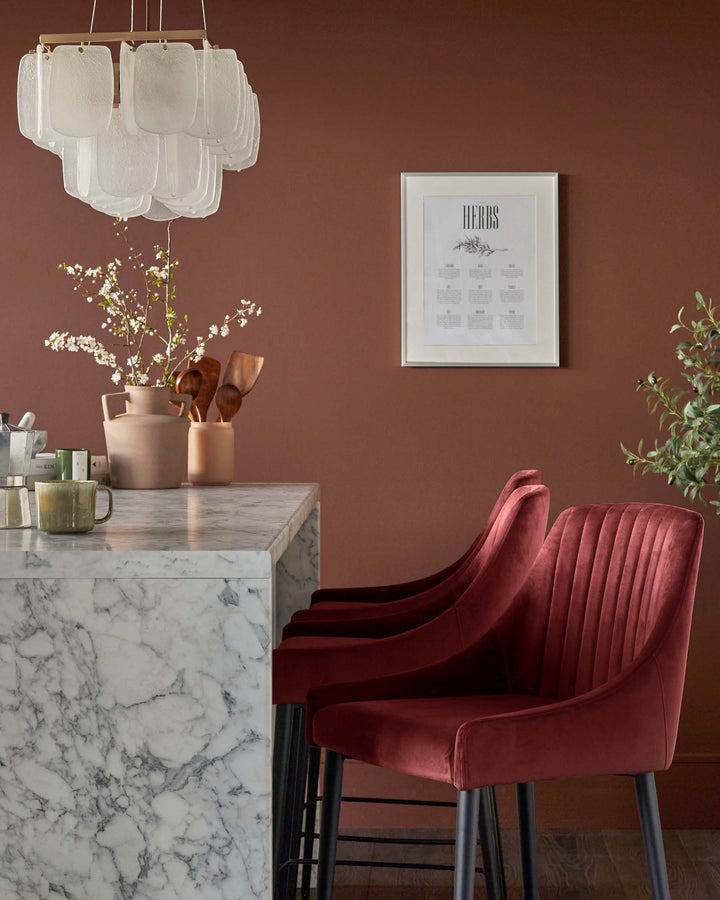 Stylish kitchen with red velvet bar stools, marble worktop, rustic vases and a modern chandelier.