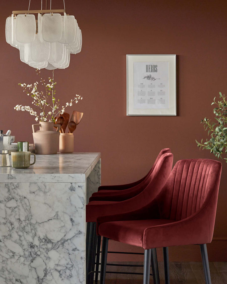 Stylish kitchen with red velvet bar stools, marble worktop, rustic vases and a modern chandelier.
