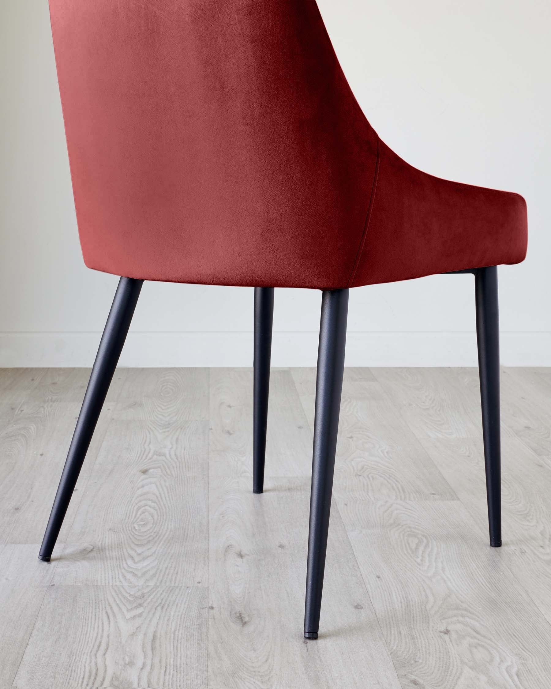 A modern, red velvet dining chair with black, tapered legs, shot from behind. Perfect for a stylish dining space.