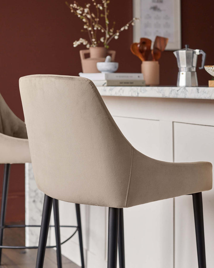Close up of a set of two upholstered bar stools in taupe with black legs against a kitchen island backdrop.