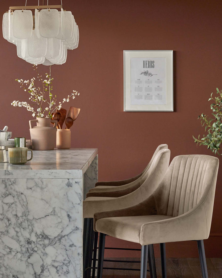 Marble-top island with upholstered bar stools in a kitchen. Statement chandelier overhead.