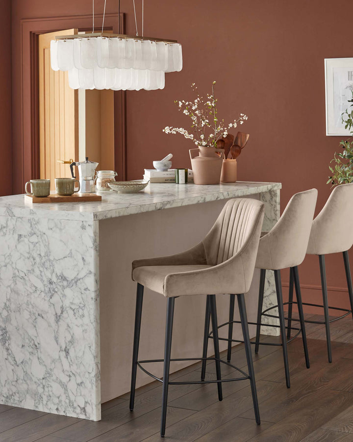 Contemporary kitchen with marble island and three stylish beige bar stools with black legs under a unique chandelier.