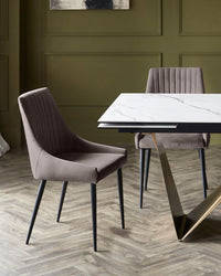 A dining set with a marble-effect table and two upholstered chairs with black legs, on a herringbone floor.