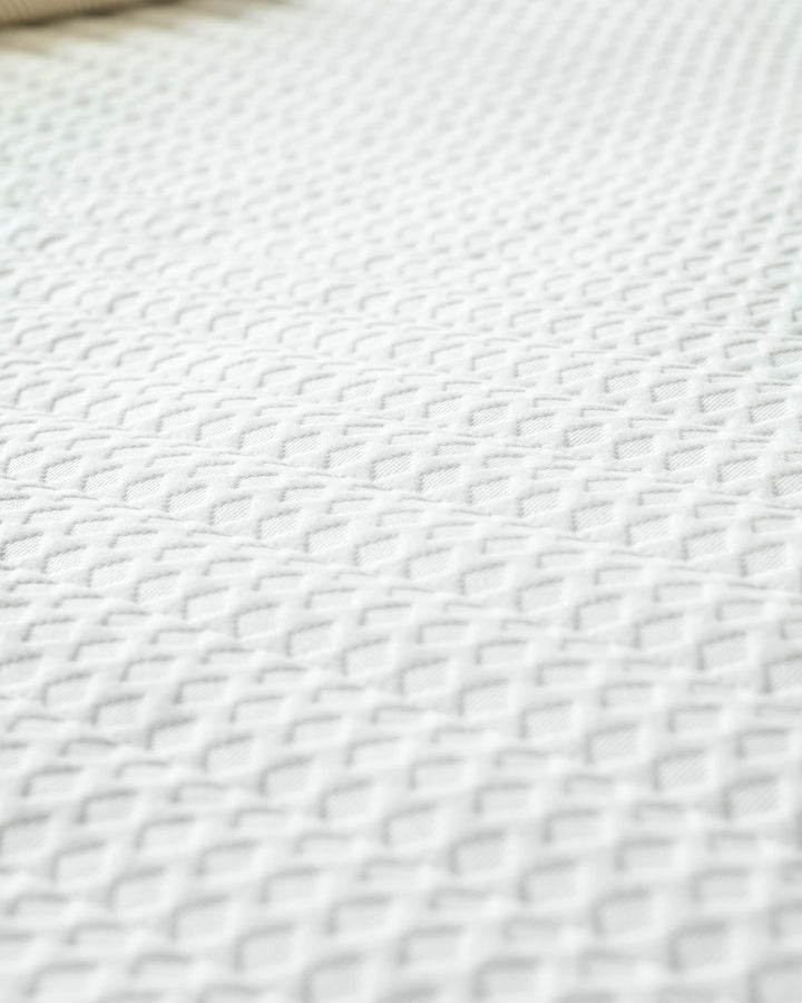 Close-up of a white textured mattress, showcasing its quality and detail. Ideal for comfortable sleep.