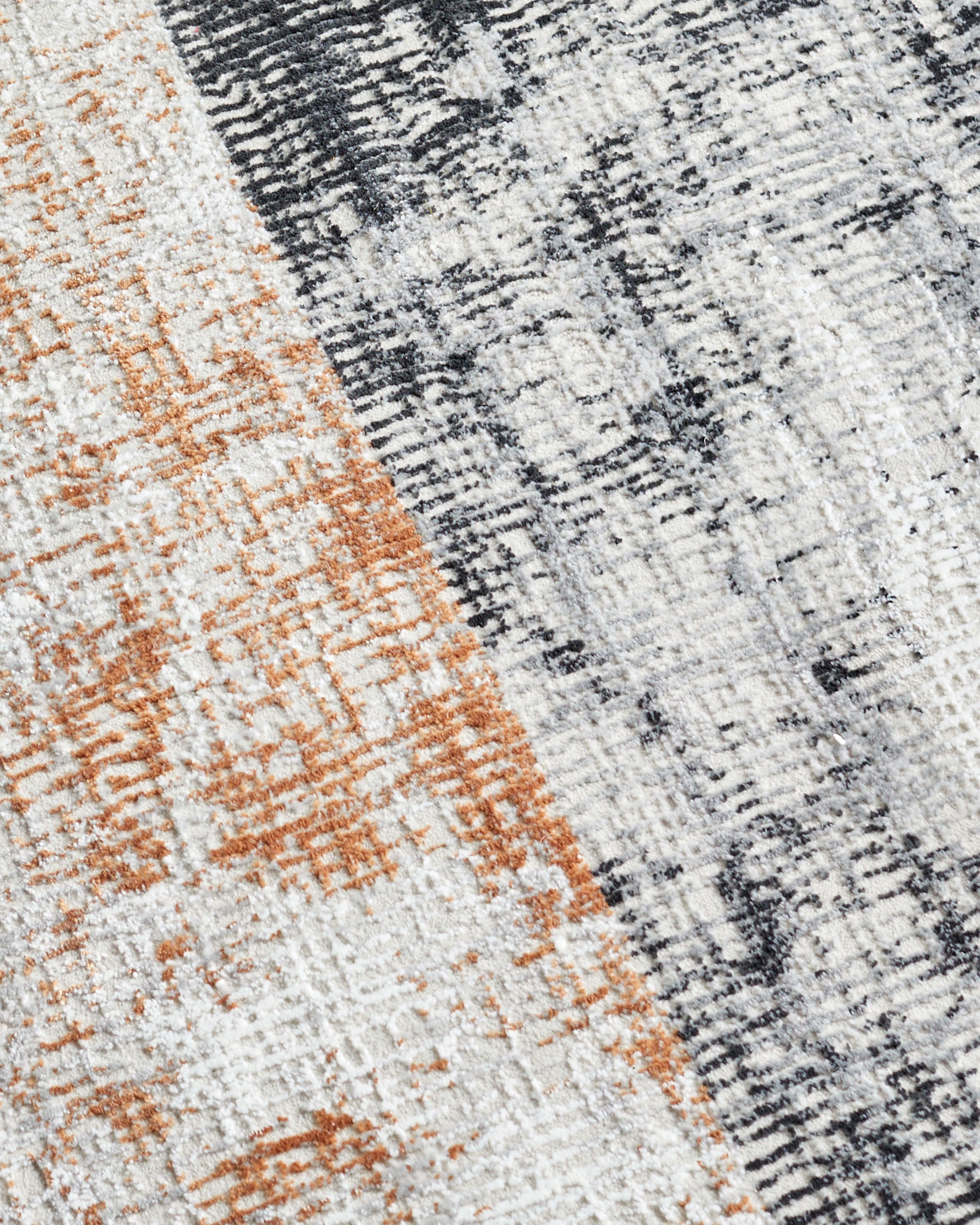 Close-up of textured rug showing terracotta and charcoal pattern with soft, blurred finish.