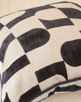 Black and cream geometric patterned cushion with curved piping detail, close-up view.