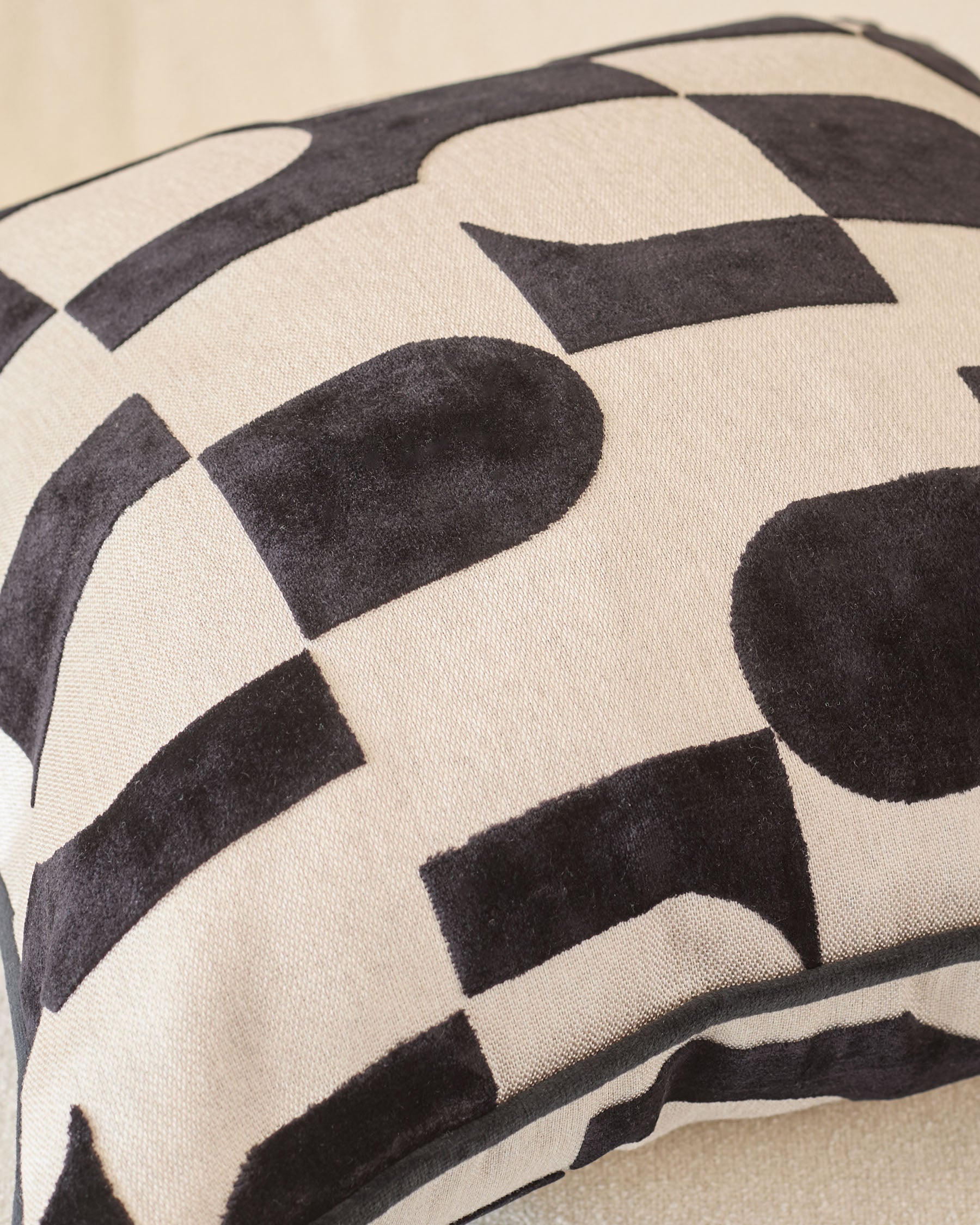Black and cream geometric patterned cushion with curved piping detail, close-up view.