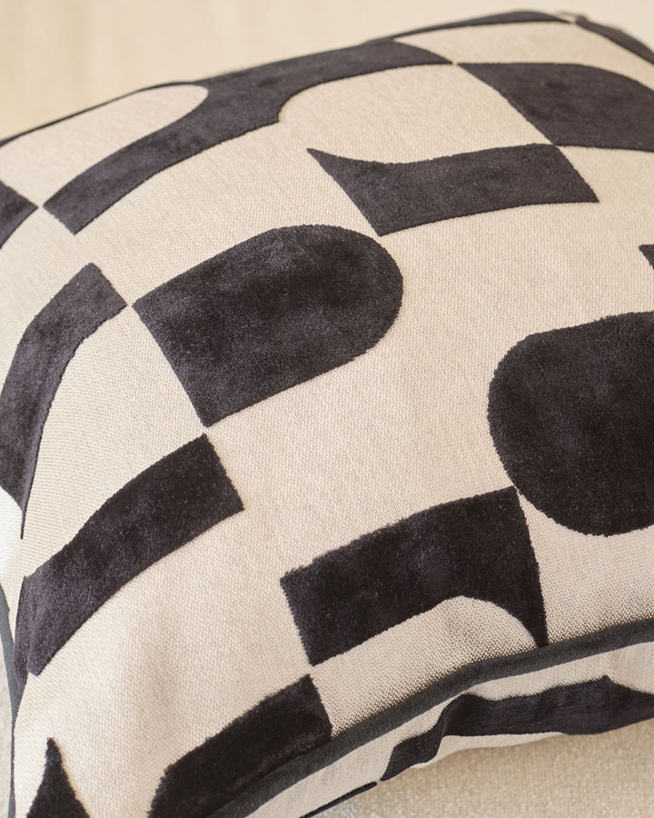 Black and cream geometric patterned cushion with curved piping detail, close-up view.