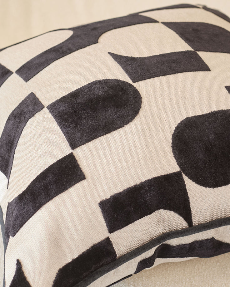 Black and cream geometric patterned cushion with curved piping detail, close-up view.