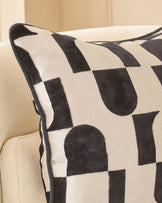 Black and cream geometric patterned cushion with piping detail, displayed on a neutral sofa.