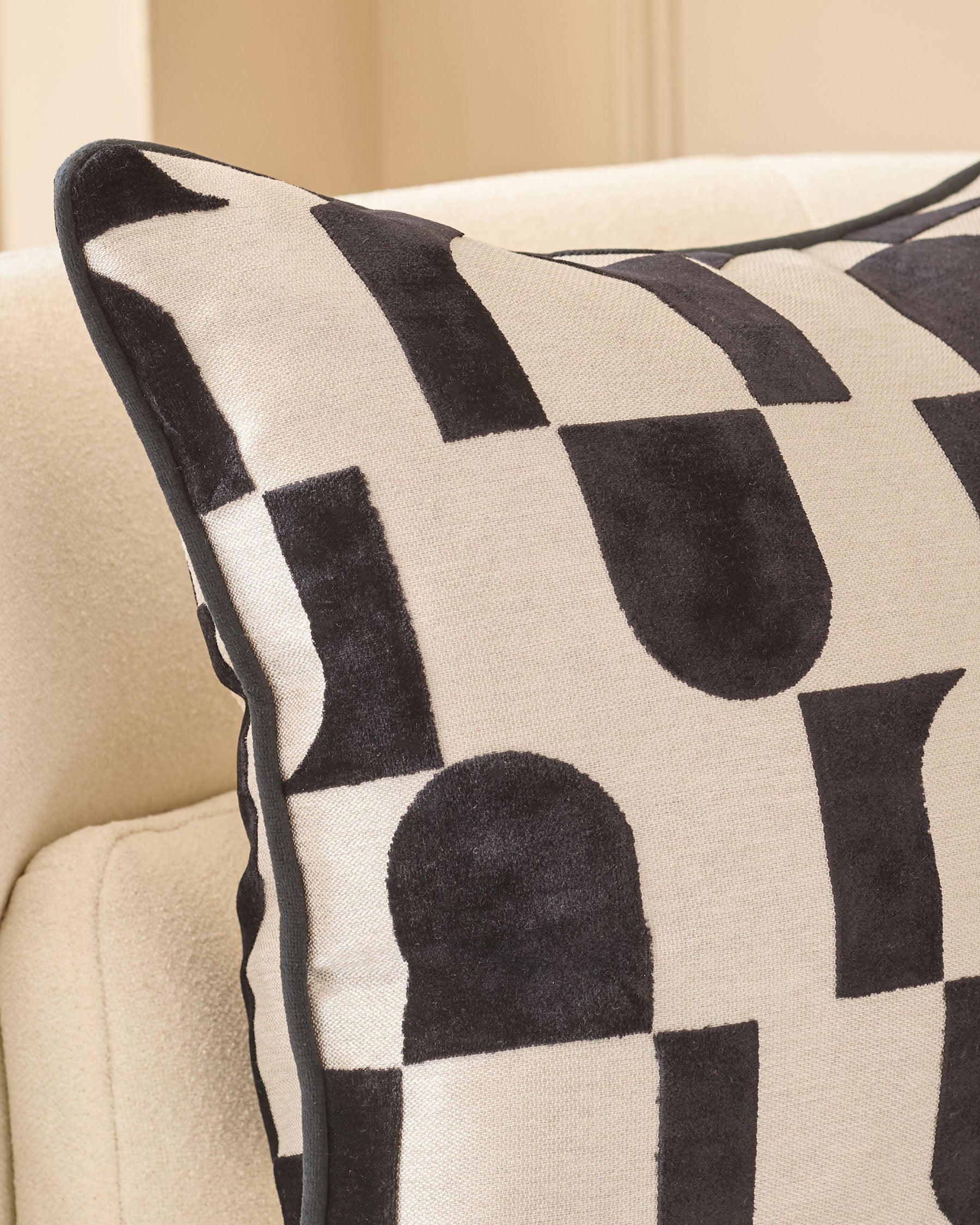 Black and cream geometric patterned cushion with piping detail, displayed on a neutral sofa.